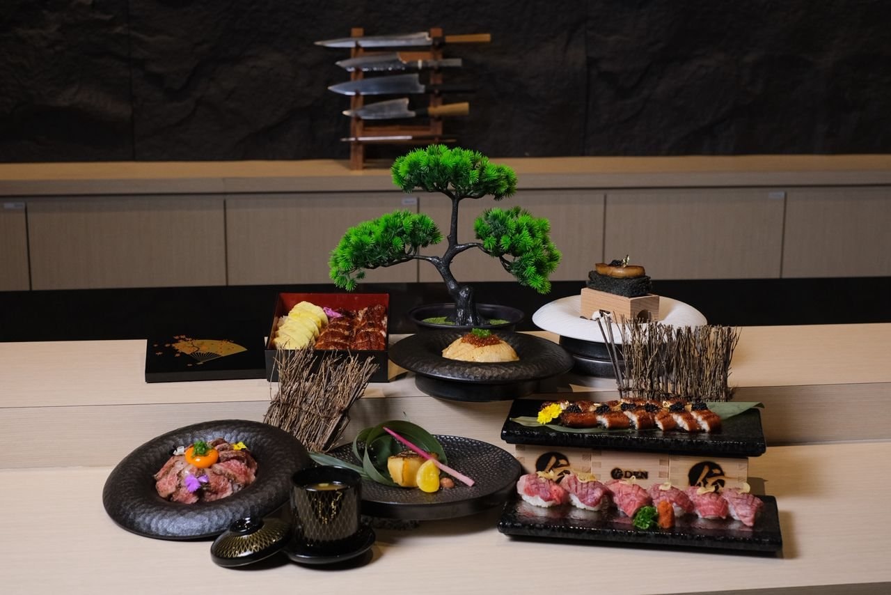 An omakase spread on the DEN Culinary counter — sashimi, wagyu nigiri and a bonsai beneath the knife rack